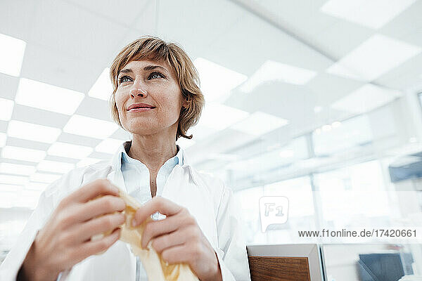 Female pharmacist with surgical glove looking away while standing at pharmacy store