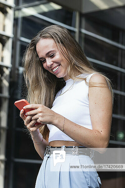 Happy blond businesswoman text messaging through mobile phone