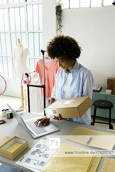 Weibliche Modedesignerin benutzt Laptop  während sie Paket im Studio hält