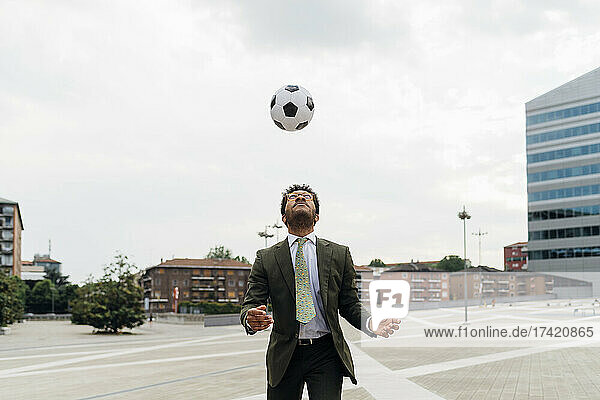 Businessman heading the ball while playing in city