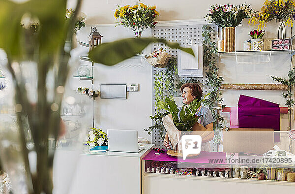 Female florist wrapping brown paper around leaves while working in flower shop