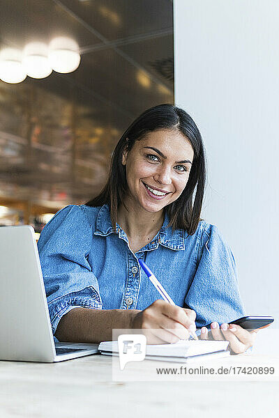 Smiling female freelancer writing on diary at cafe