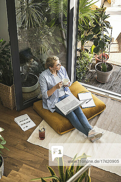 Geschäftsfrau trinkt Kaffee  während sie zu Hause mit Tagebuch und Laptop sitzt
