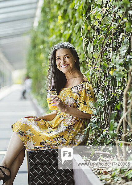 Smiling beautiful mature woman sitting with jar in front of plants