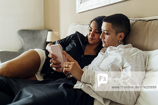 Queer couple using phones while lying on bed at home