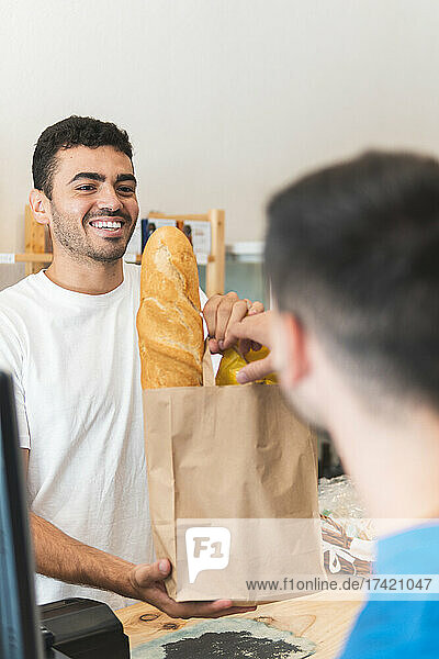 Happy male entrepreneur giving shopping bag to customer at shop