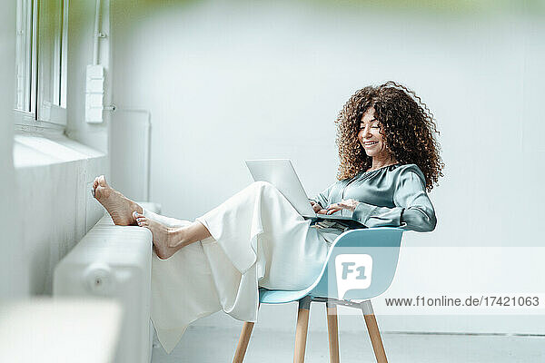 Geschäftsfrau benutzt Laptop  während sie im Büro auf einem Stuhl sitzt