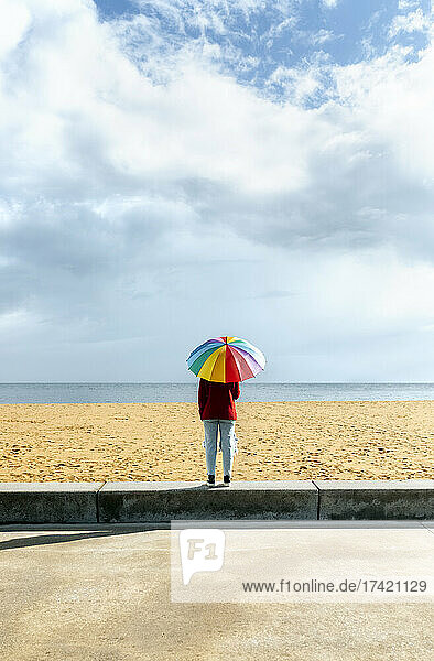 Mid adult woman standing with multi colored umbrella at beach