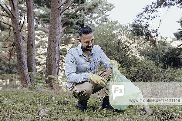 Männlicher Hipster-Umweltschützer sammelt Plastik beim Säubern des Waldes