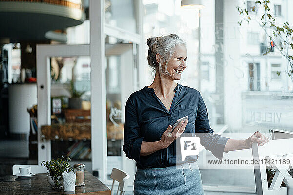 Businesswoman with mobile phone standing at cafe table