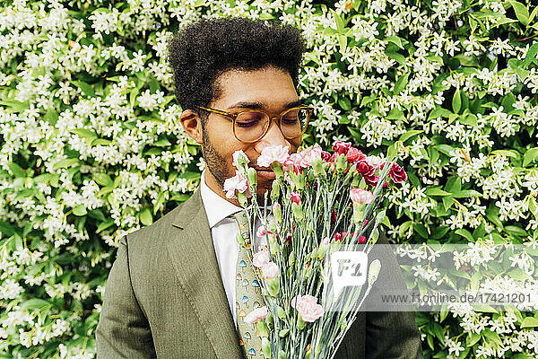 Businessman smelling bouquet in front of flowering plants