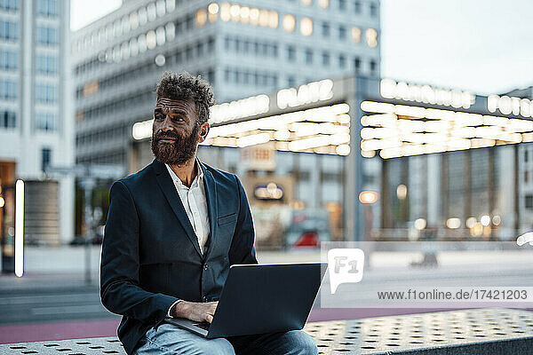 Businessman with laptop sitting on bench at station