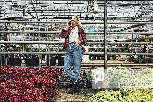 Smiling female farmer with hand in pocket talking on mobile phone at plant nursery