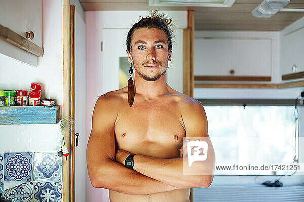 Confident shirtless man standing with arms crossed in motor home