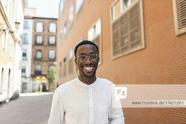 Young man in eyeglasses smiling in front of buildings