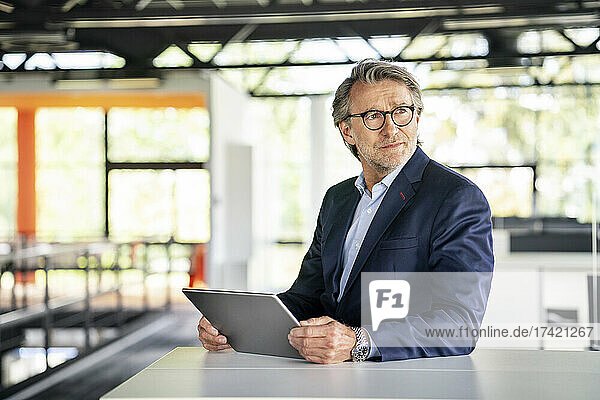 Mature businessman holding digital tablet at desk in office