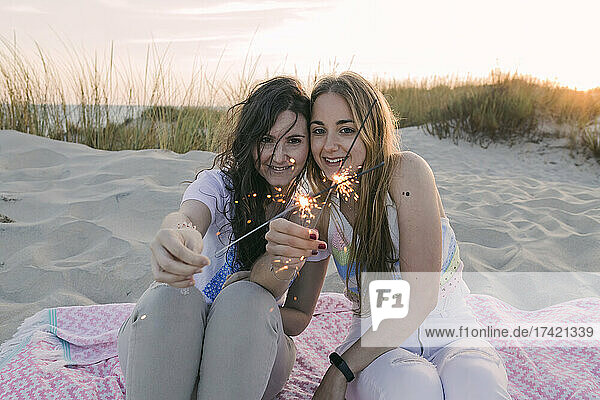 Young female friends burning sparklers at beach