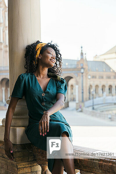 Smiling young woman looking away while leaning on column  Plaza De Espana  Seville  Spain