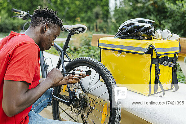 Young delivery man inflating bicycle by bench