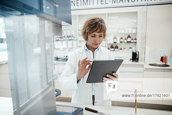 Female pharmacist using digital tablet while standing at laboratory