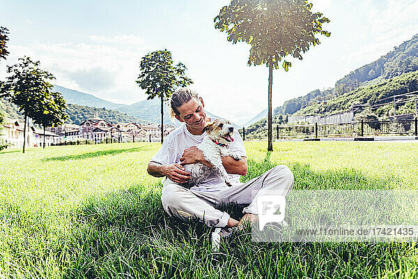 Mid adult man with pet dog sitting cross-legged on grass