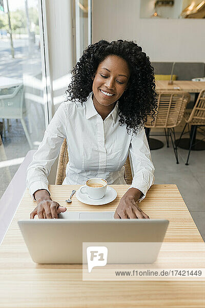 Lächelnde Geschäftsfrau benutzt Laptop  während sie am Cafétisch sitzt