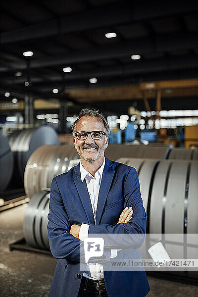 Smiling male professional with arms crossed standing at mental industry