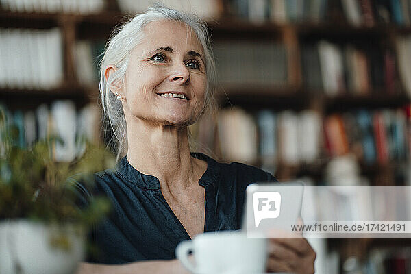 Smiling mature businesswoman holding mobile phone in cafe