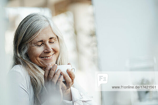 Smiling woman with eyes closed holding coffee cup in cafe