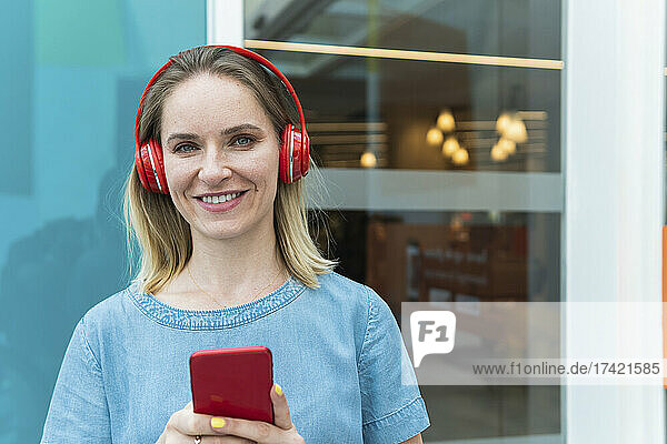 Smiling businesswoman wearing wireless headphones holding mobile phone