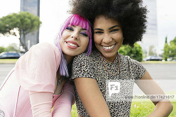 Woman with dyed hair leaning on Afro female friend at park