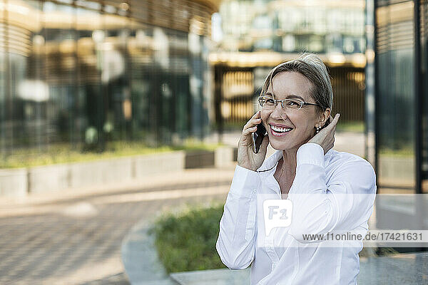 Cheerful businesswoman with hand in hair talking on mobile phone