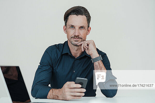 Mature businessman with smart phone and laptop in office