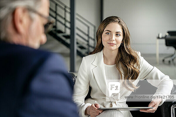 Beautiful businesswoman with digital tablet looking at male professional in office