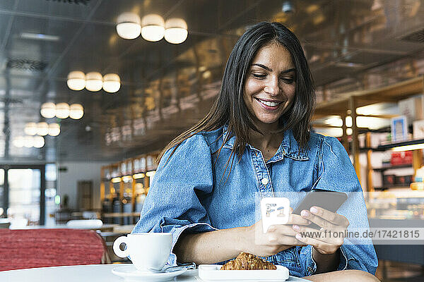 Lächelnde Geschäftsfrau benutzt Mobiltelefon  während sie im Café sitzt