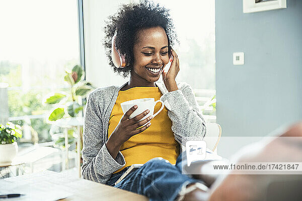 Happy woman listening music through headphones while having coffee at home