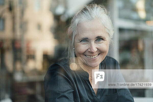Lächelnde Frau  die durch das Caféfenster schaut