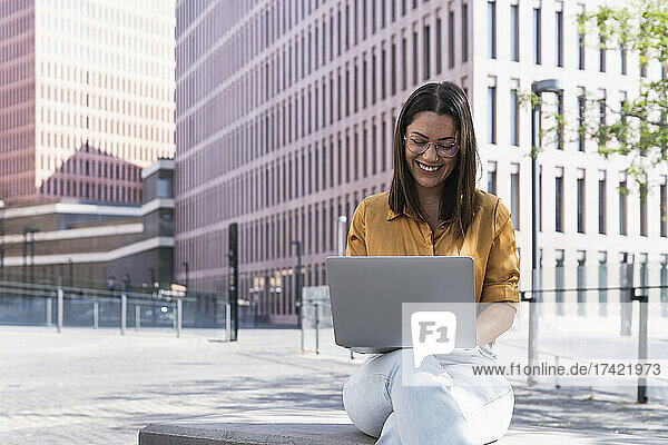 Smiling female professional using laptop on bench at office park