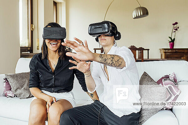 Young lesbians gesturing while enjoying virtual reality through headsets at home