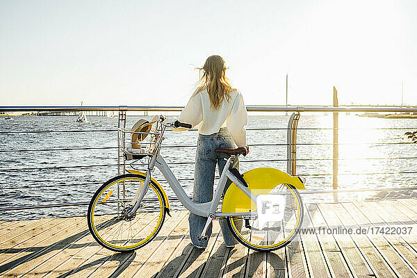 Woman with bicycle looking at sea while standing at boardwalk