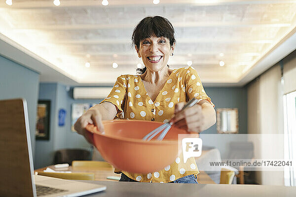 Aufgeregt reife Frau  die zu Hause in der Küche lernt  über Laptop Essen zuzubereiten