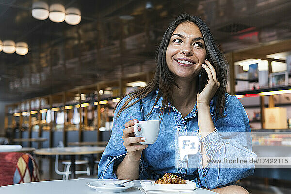 Businesswoman with coffee cup smiling while talking on smart phone at coffee shop