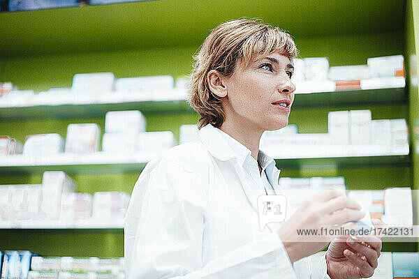 Female pharmacist with short hair holding medicine at pharmacy store