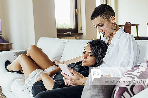 Queer woman showing mobile phone to girlfriend at home
