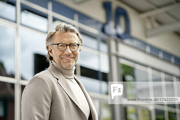 Reifer Geschäftsmann mit Brille steht vor dem Gebäude im Büropark