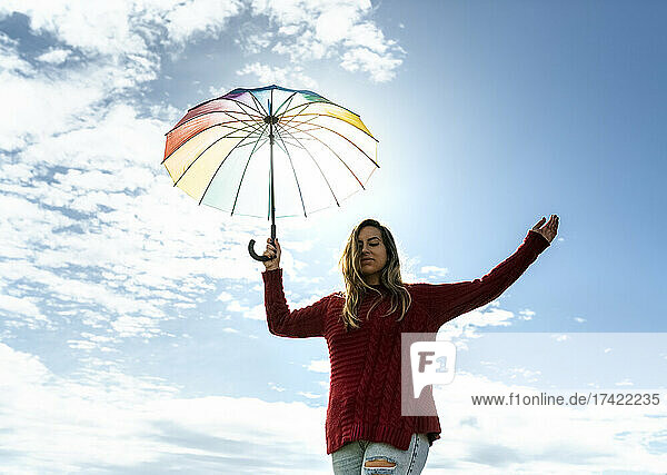 Woman holding umbrella while walking in front of cloudy sky