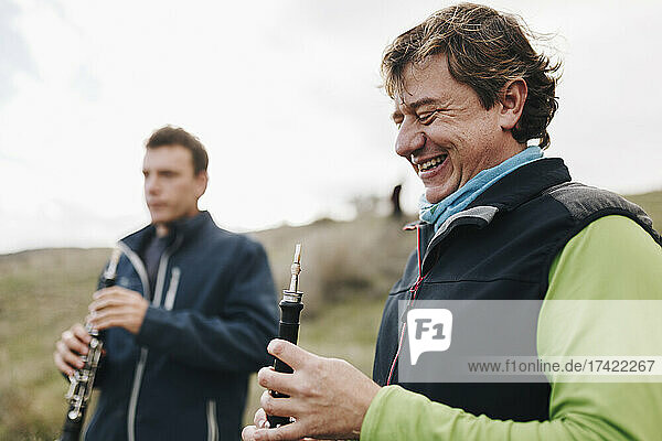 Happy man looking at musical instrument with male friend in background