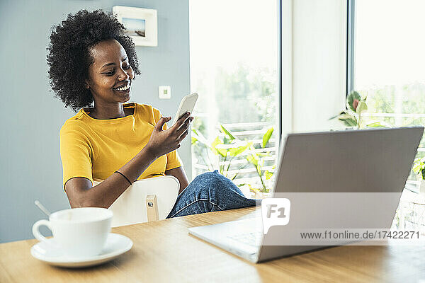 Afro female professional using mobile phone while sitting on chair at home
