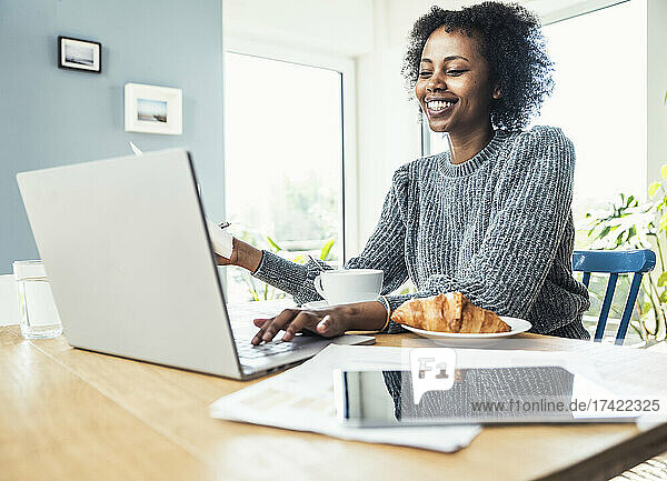 Smiling female freelancer using laptop during video conference at home office