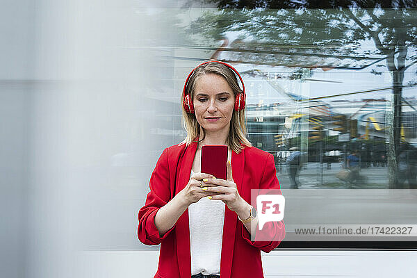 Geschäftsfrau trägt kabellose Kopfhörer und nutzt ihr Smartphone